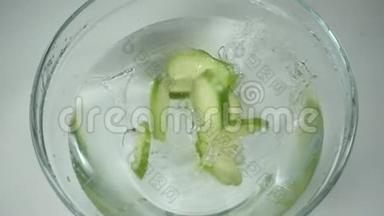 黄瓜片在厨房的一个玻璃碗水，慢动作。 新鲜黄瓜片上的清水溅出