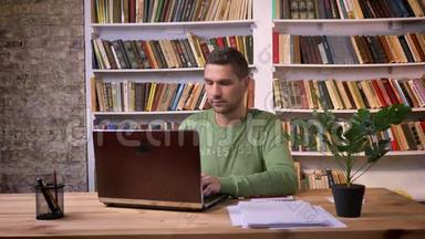 成年男子在<strong>办公室</strong>工作的金属笔记本电脑。 <strong>背景书架</strong>