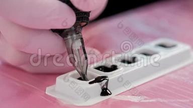 纹身师傅在纹身机里<strong>拿起</strong>墨水。 红色背景上的粉红色安全手套。