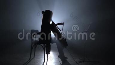 女孩晚上在烟雾弥漫的房间里鞠躬大提琴。 剪影。 黑烟背景