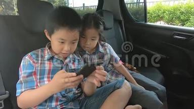 快乐的小男孩女孩戴着安全带在车里拿着智能手机