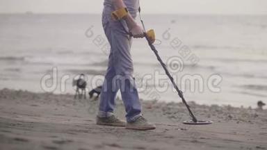 无法辨认的人带着电子金属探测器在海滩上用金属探测器扫描沙子，发现贵重物品。