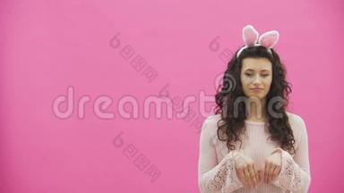 年轻漂亮的夫妇站在粉红色的背景上。 在这期间，他们做兔子的动作。 女人把她