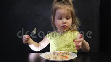 孩子们在黑桌上用勺子在黑色背景上吃煮熟的米饭和蘑菇