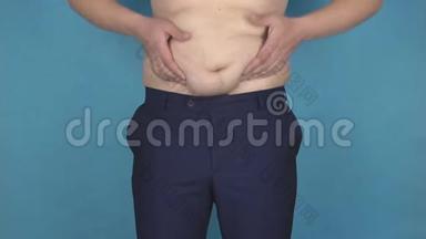 一个年轻人在厚厚的反脂肪胃上摩擦他的脂肪皱褶，这是一种错误的生活方式和营养的概念