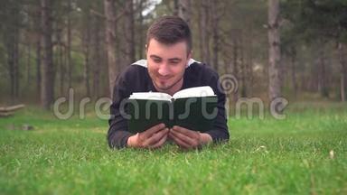 一个年轻人躺在森林里的绿草上看书。 休息，放松，愉悦..