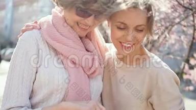 女儿和母亲通过智能<strong>手机</strong>上的照片。 春天阳光明媚的街道上的肖像。 母亲<strong>节</strong>
