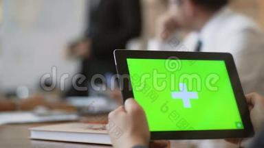 在办公室的一次会议上，一位特写员工拿着一块绿色屏幕的平板电脑