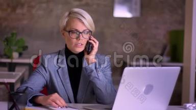 戴眼镜的金发短发女商人在办公室里用手机<strong>认真</strong>说话的肖像。