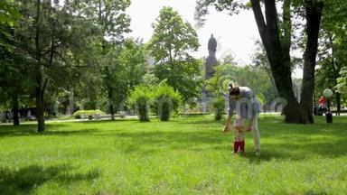 可爱的苗条妈妈帮助她漂亮的滑稽女儿在画城公园的绿草上迈出第一步