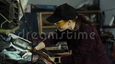 漂亮的女机械师，深色头发，穿着格子衬衫和帽子，戴着<strong>防</strong>护<strong>眼镜</strong>修理汽车发动机。 概念