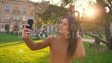美丽的黑发美女在绿色公园背景下使用智能<strong>手机制作</strong>自拍照片的肖像。