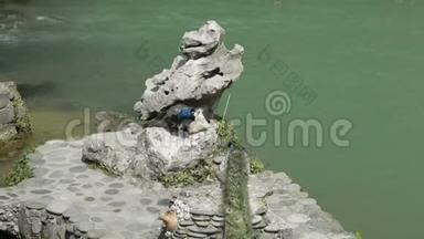 孔雀坐在石头上，孔雀用绳子绑在石头上，游客用孔雀拍照