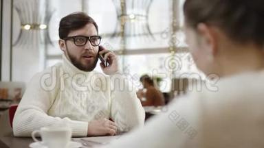 年轻的商人正和他的女朋友一起坐在餐馆的桌子旁谈论他的智能手机