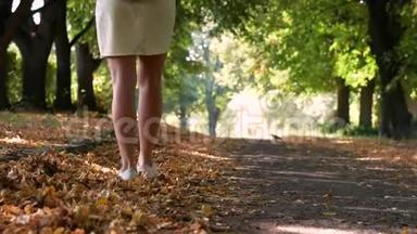一个女孩在公园里散步和踢落叶。 优雅的女人穿<strong>白色短裤</strong>。 金秋概念