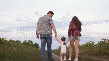 小女儿跳着手牵着爸爸妈妈。 一家人带着小孩走在路上，在田野旁欢笑