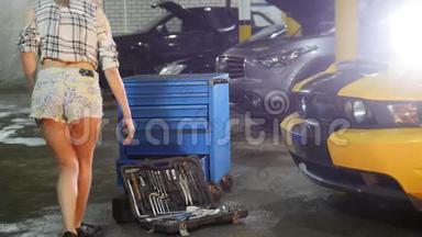 汽车修理服务。 穿小短裤的年轻女子走到工具箱前，弯下腰，拿起扳手