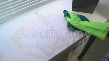 一只手戴绿色防护手套，用蓝色潮湿的抹布清洗窗台，使其不受灰尘和污垢的影响。