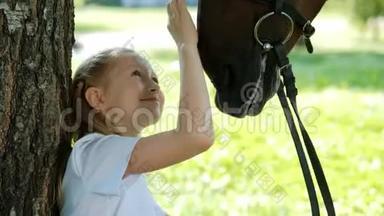 少女骑师坐在树下的绿色空地上。 给一匹马一个苹果，然后<strong>抚摸</strong>它。