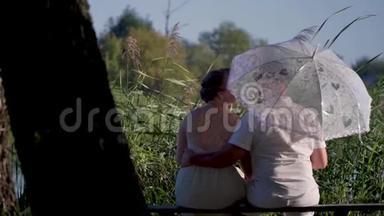 女人和她的<strong>爱人</strong>拿着白伞坐在河边的长凳上