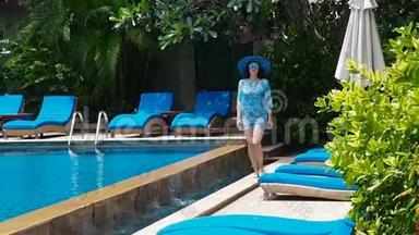 在阳光明媚的日子里，穿着蓝色泳衣、帽子和<strong>太阳镜</strong>的漂亮<strong>女士</strong>带着清澈的水在游泳池里走来走去。 奢华