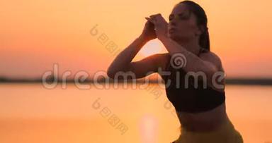 从侧面看年轻女人在户外蹲。 站在湖边的年轻健身女子蹲着蹲着