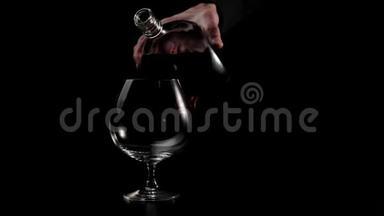 豪华白兰地。 穿着黑色衬衫的人从一个圆形的瓶子里倒入一个黑色背景的杯子里。 白兰地，白兰地。