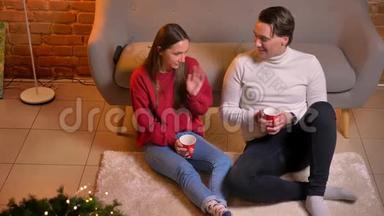 从上往下看，快乐的白种人朋友坐在地毯上喝茶，在圣诞节的家庭氛围中交流。