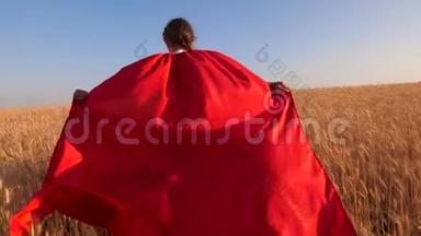孩子穿着漂亮的红色斗篷，在蓝天上跑过麦田。 特写镜头。 少女扮演红色超级英雄