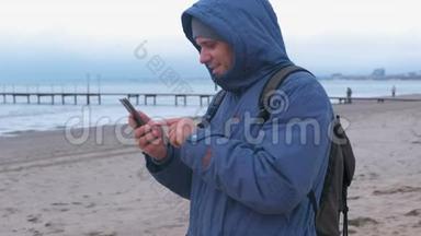 穿着蓝色羽绒服的人在海边的沙滩上打手机留言。 侧视。