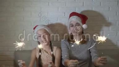 戴着圣诞老人帽子的快乐、快乐的孩子们手里拿着点燃的火花，挥手，坐在沙发上微笑