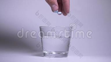 男人的手把两片蓝色泡腾药片扔进一杯水中。慢动作。药丸在水中溶出气泡。