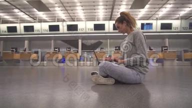 女孩坐在机场地板上的候机楼里，在等待航班时用笔记本电脑工作。