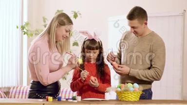 女孩拿着一个复活节彩蛋，爸爸妈妈在上面画。