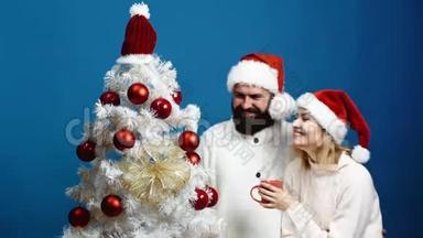 可爱的一对幸福的夫妇在<strong>圣诞</strong>树旁<strong>迎</strong>接新年。 一对年轻夫妇戴着新年`帽子装饰<strong>圣诞</strong>节