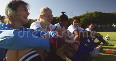 快乐多样的女足球员坐在足球场上交谈。 4k