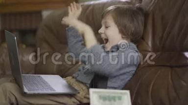 肖像可爱的小男孩坐在皮革沙发上，腿上有笔记本电脑，在空中扔钱