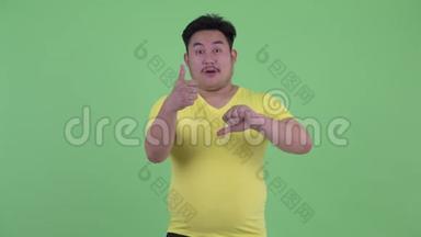 一个困惑的、超重的亚洲年轻人在竖起大拇指和竖起大拇指之间做出选择