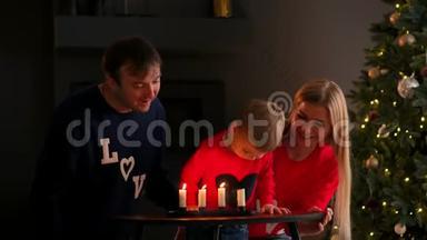 一家人在圣诞节坐在树下看着孩子吹灭蜡烛，笑。 妈妈爸爸笑着