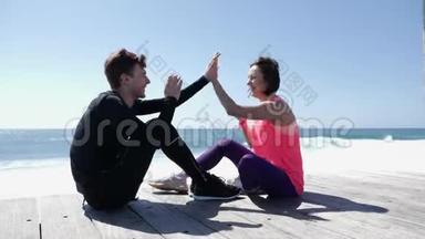 快乐的年轻男友和女友坐在海边玩击掌游戏。 海浪拍打着岩石