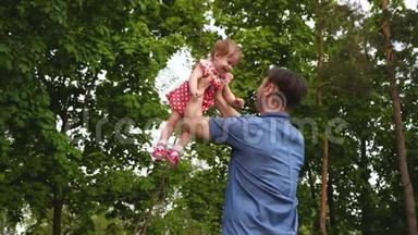 当小女儿在怀里在空中旋转时，她和父亲一起笑。 在公园里散步和玩耍