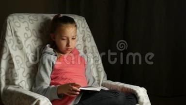 穿灰色粉红色运动衫的可爱的<strong>女孩子</strong>坐在房间里舒适的椅子上看书