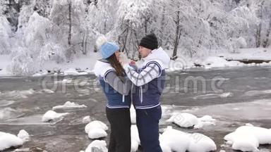 恋爱中的情侣在一条奔腾的山河的河岸上，在冬日的森林里欢笑和拥抱。