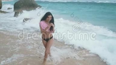 慢动作运动的快乐女孩穿着泳装在海浪中沿着海滩散步，Stealicam射击