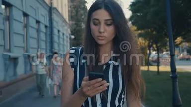 年轻漂亮女人的正面视图检查智能手机内容并沿着市中心走下去。