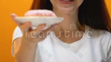 满意的漂亮女孩在镜头中显示粉红色釉面甜甜圈，<strong>糖尿病</strong>的风险
