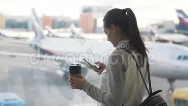 侧景女孩用手机和饮料外卖咖啡<strong>在机场</strong>背景的飞机<strong>在</strong>窗口