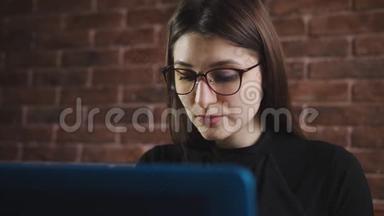 带眼镜的年轻女孩正在办公室的笔记本电脑键盘上打字。 年轻记者在电脑键盘上打字