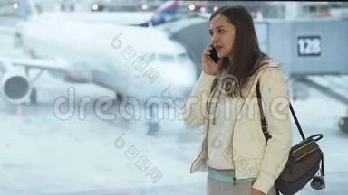 穿着运动服和背包的女孩站<strong>在机场</strong>的窗口，<strong>在</strong>飞机背景上打电话