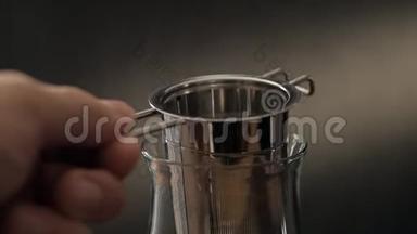 用金属<strong>过滤</strong>器在玻璃杯中酿造茶。 一个男人的特写`手把茶倒进茶<strong>过滤</strong>器。